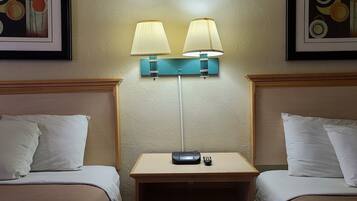 A hotel room with two beds, a nightstand with a lamp, and artwork on the walls.