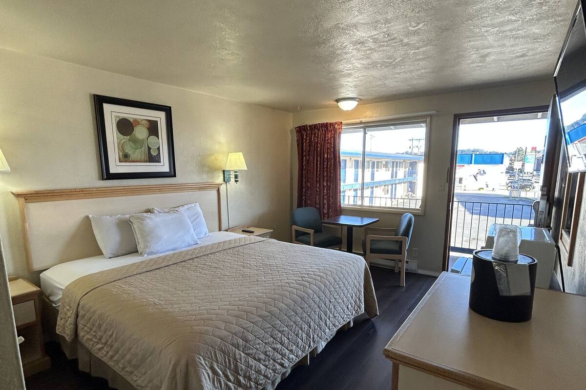 Ein Hotelzimmer mit Bett, Schreibtisch, Stuhl, Fenster mit Blick und einem gerahmten Bild an der Wand.
