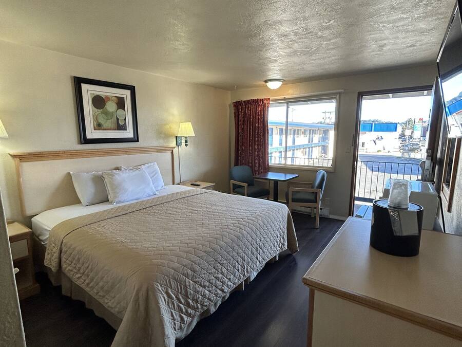A hotel room with a bed, a desk, a chair, a window with a view, and a framed picture on the wall.
