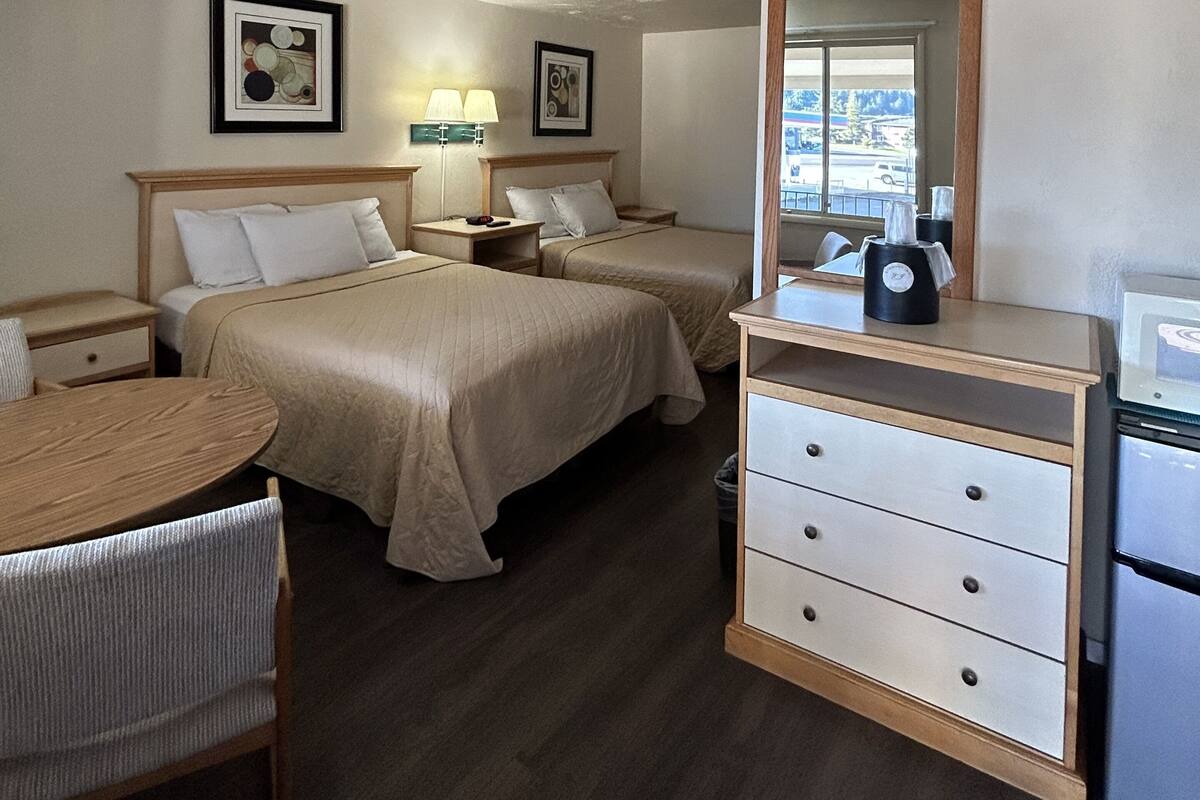 Ein Hotelzimmer mit zwei Betten, einem Schreibtisch, einem Stuhl, einem Schminktisch und zwei gerahmten Bildern an der Wand.