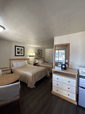 A hotel room with two beds, a desk, a chair, a dresser, a mirror, and two framed pictures on the wall.