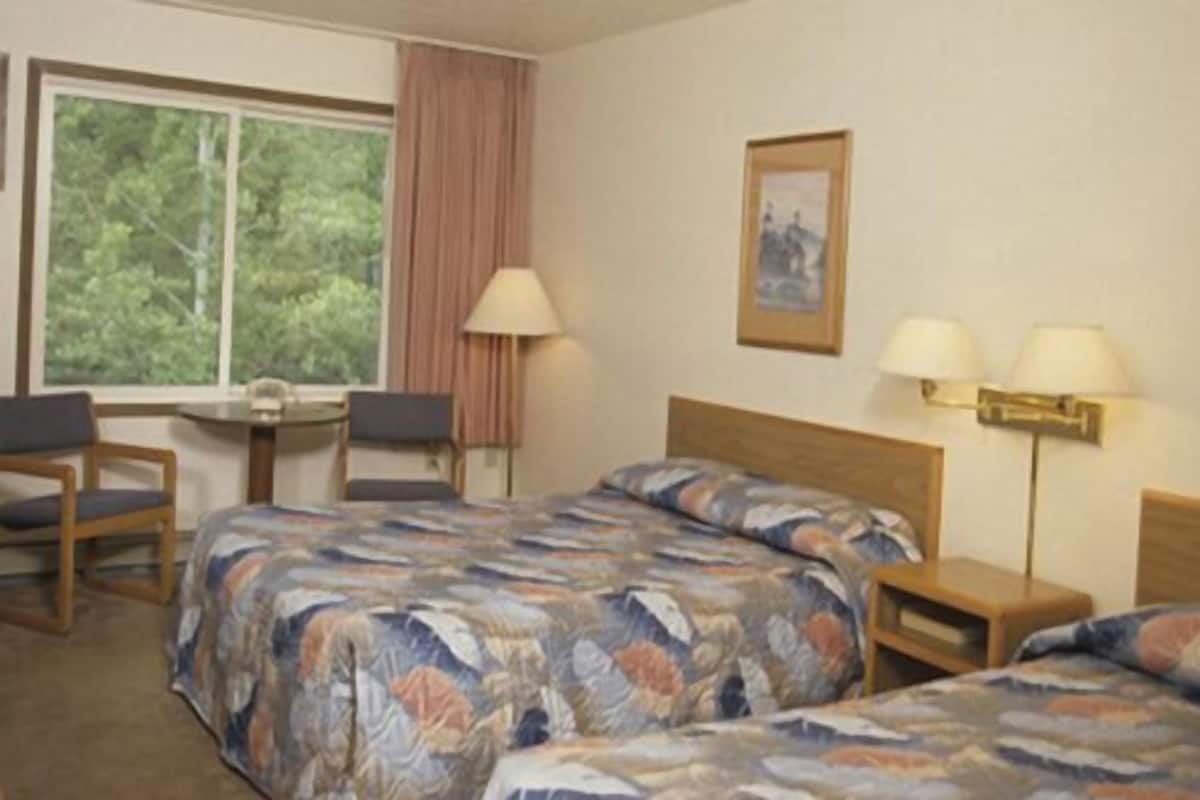 A hotel room with two beds, a desk, a chair, and a window with curtains.