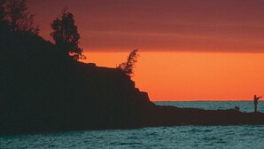 A person fishing at sunset on a rocky coastline. - Aspen Inn (Grand Marais)