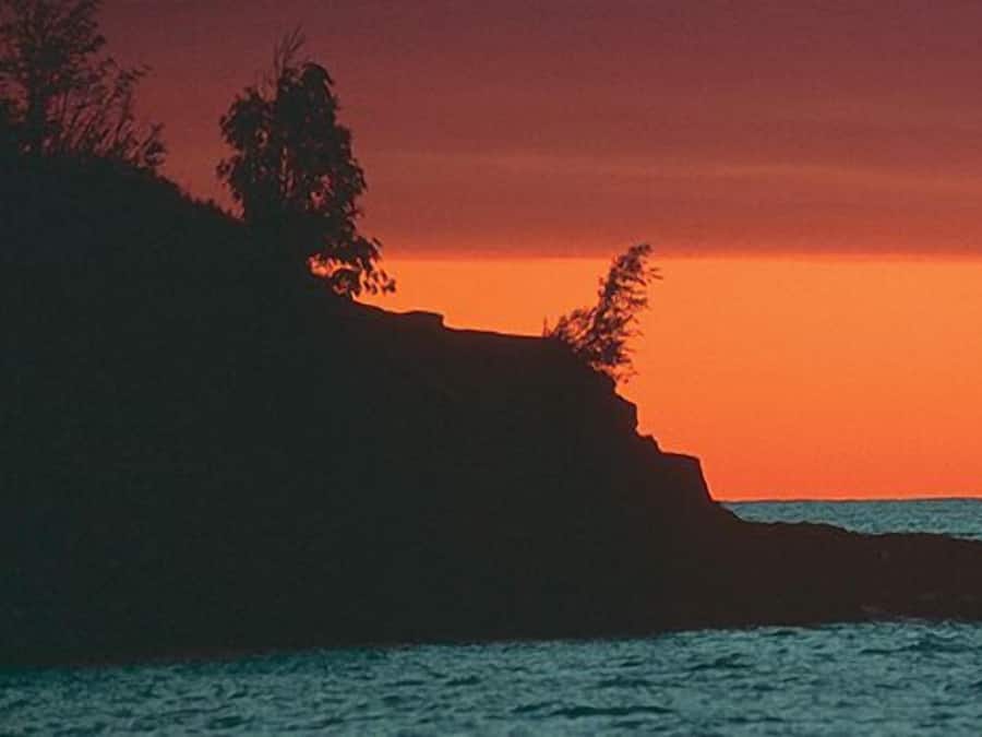 Henkilö kalastaa auringonlaskun aikaan kivikkoisella rannikolla.