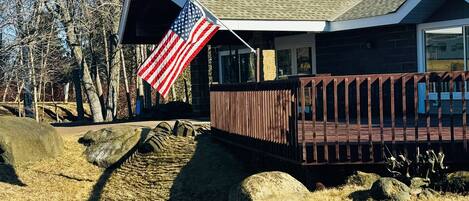 A building with a sloped roof, an American flag, a wooden deck, and a stone wall.