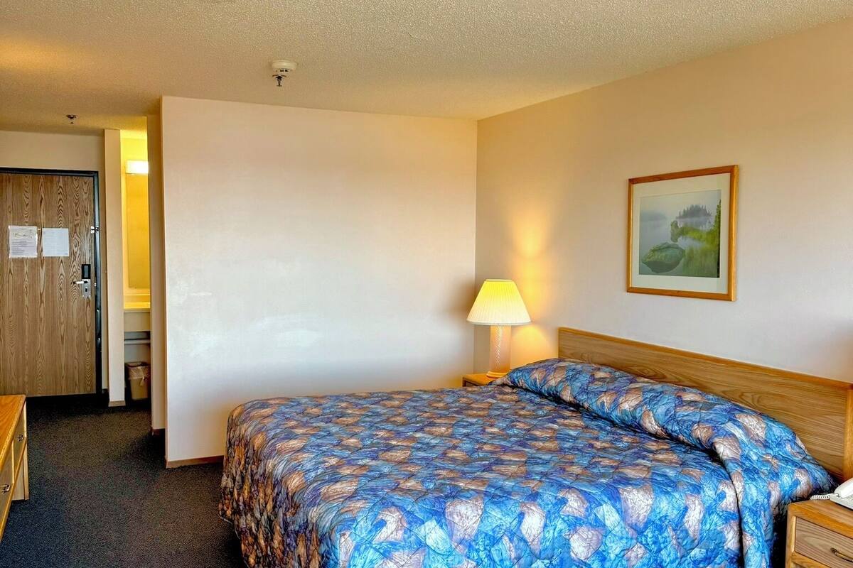 Habitación de hotel con una cama, un escritorio, una lámpara y un cuadro en la pared.