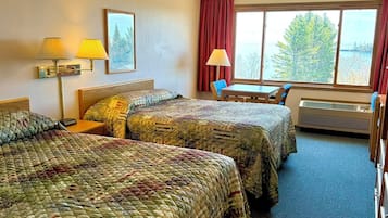 Habitación de hotel con dos camas, una mesa, sillas, un ventanal y una lámpara.
