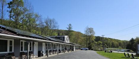 A row of motel-style buildings with attached parking, a paved road, and a grassy area with lounge chairs.
