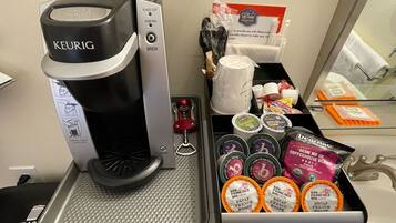 Una macchina per caffè Keurig con un vassoio raccogligocce, un portacaffè con diversi tipi di capsule, e un ripiano con bicchieri usa e getta e una confezione di caffè.