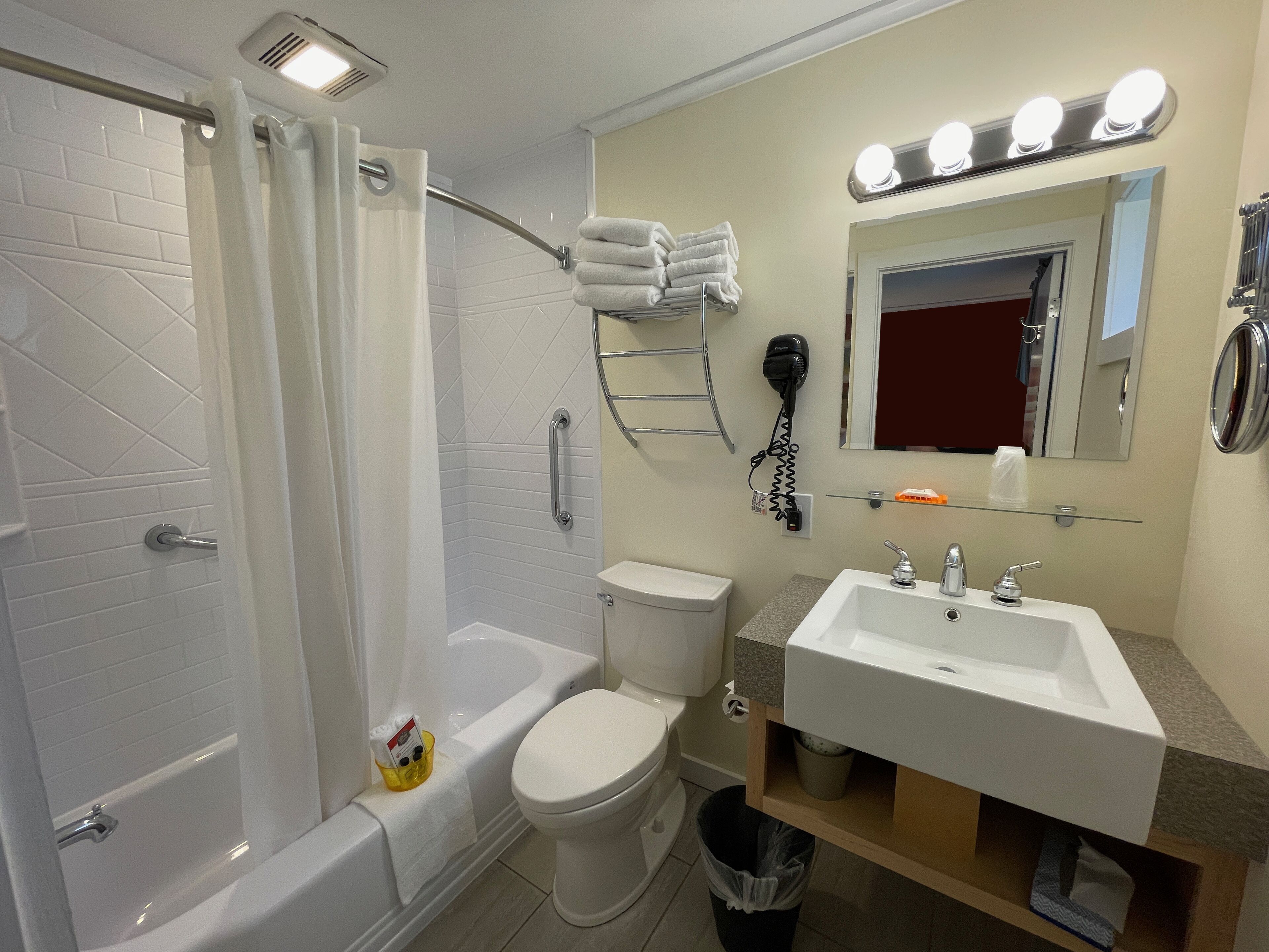 A bathroom with a bathtub, toilet, sink, and a vanity mirror with lights.
