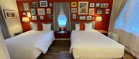 A hotel room with two beds, a window with curtains, and a wall decorated with framed pictures.