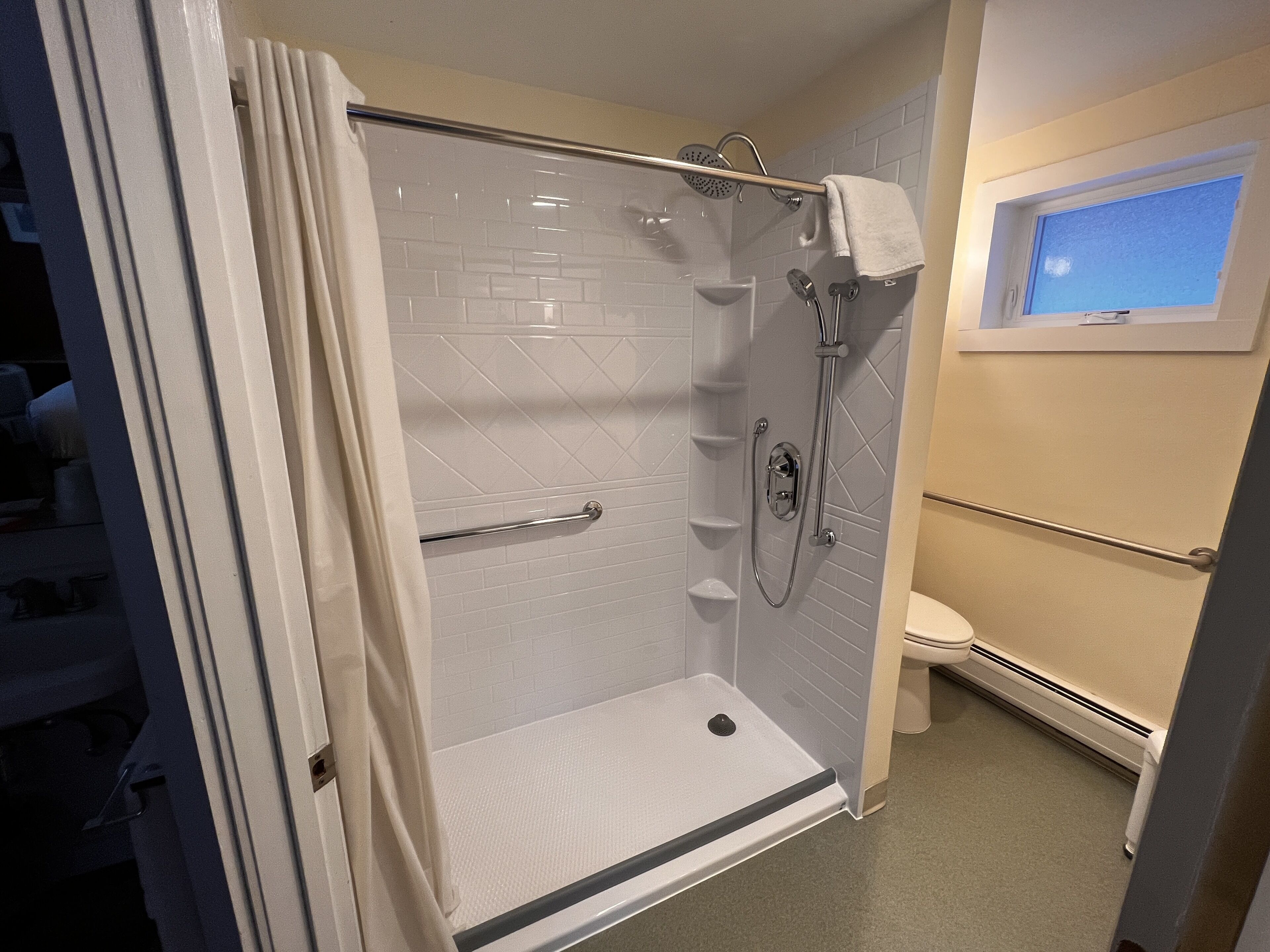 Een inloopdouche met een glazen deur, een handdoekhouder en een raam boven het toilet.