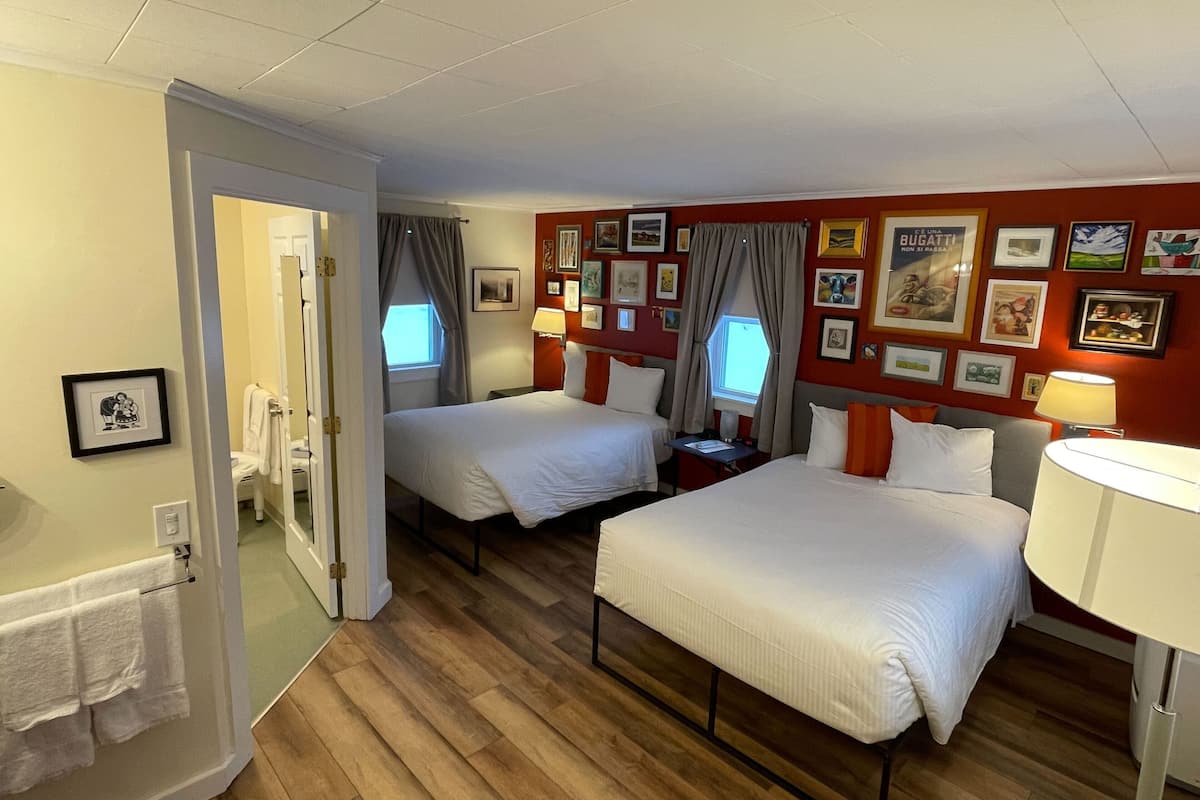 Een hotelkamer met twee bedden, een badkamer en een gang.