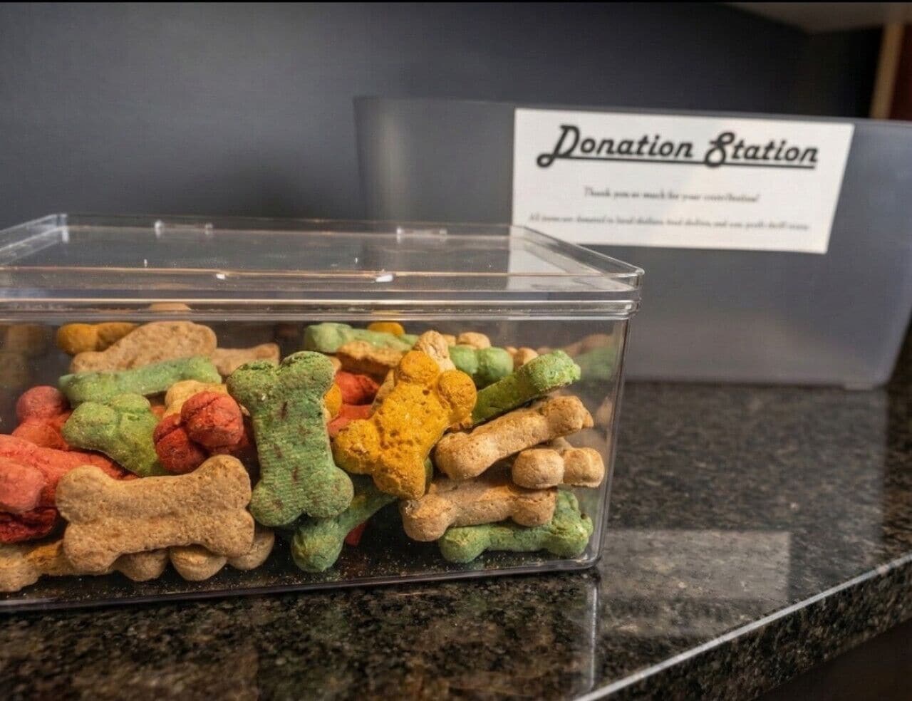 A donation station with a sign, and a container filled with colorful dog-shaped treats.