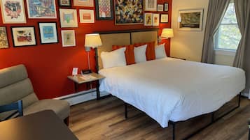 A hotel room with a large bed, a chair, a table, and a wall decorated with framed artwork.