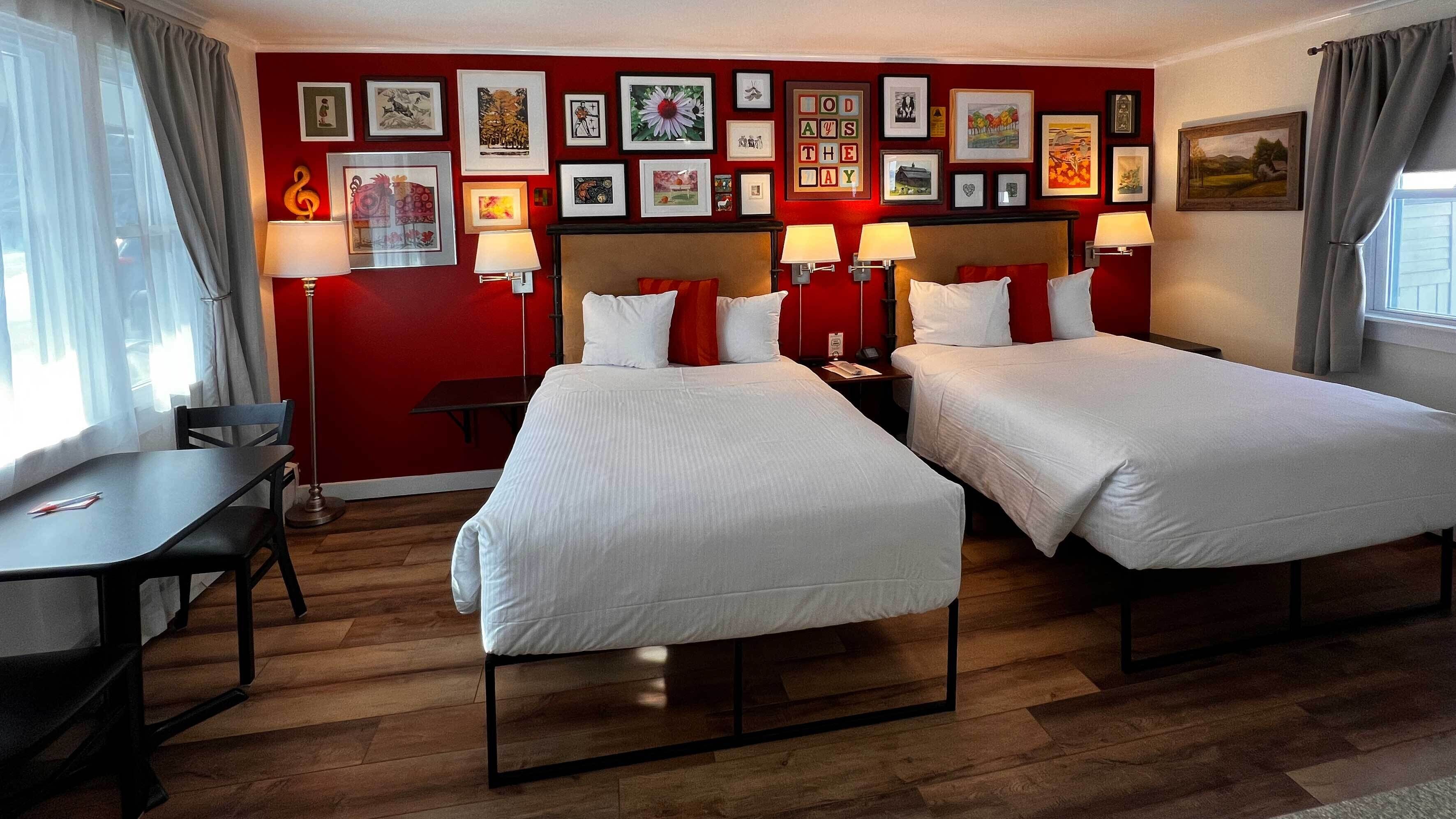 A hotel room with two beds, a desk, and a chair. There are multiple framed pictures on the wall.