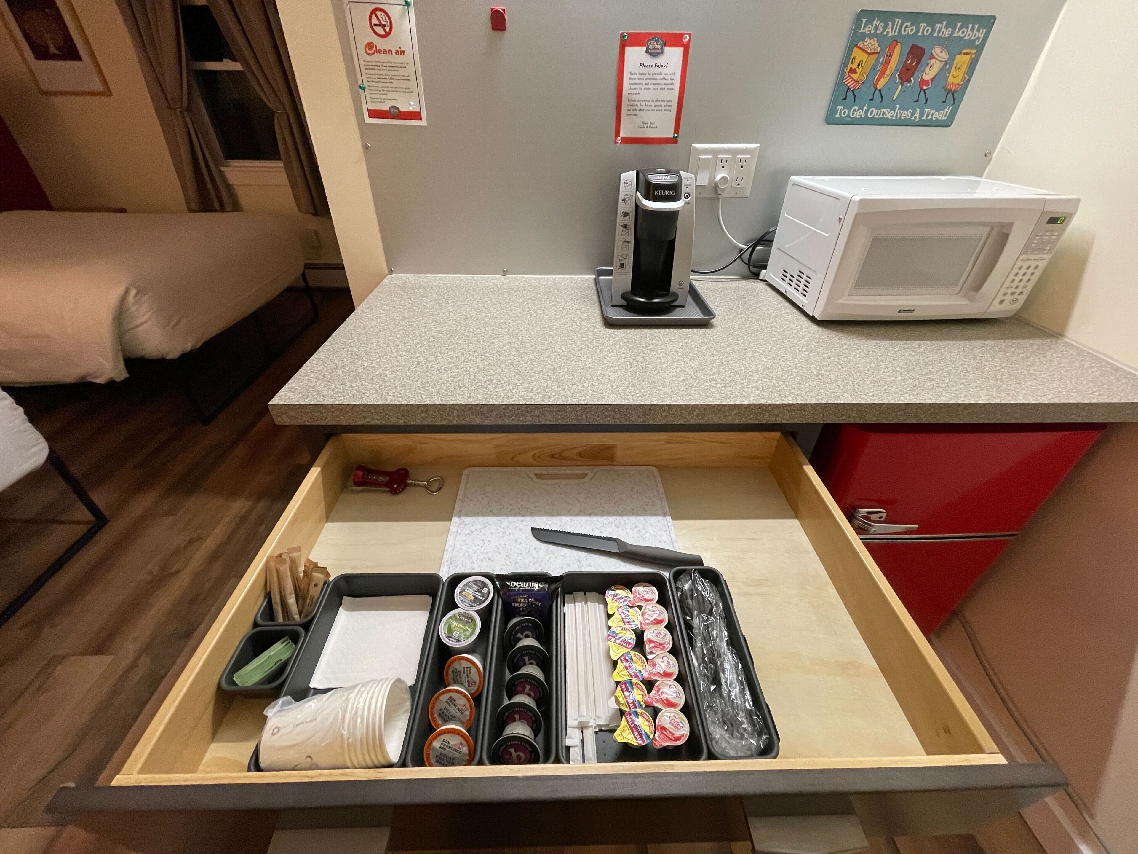 Une petite cuisine équipée d’une machine à café, d’un four à micro-ondes et d’un tiroir contenant des ustensiles et des en-cas.