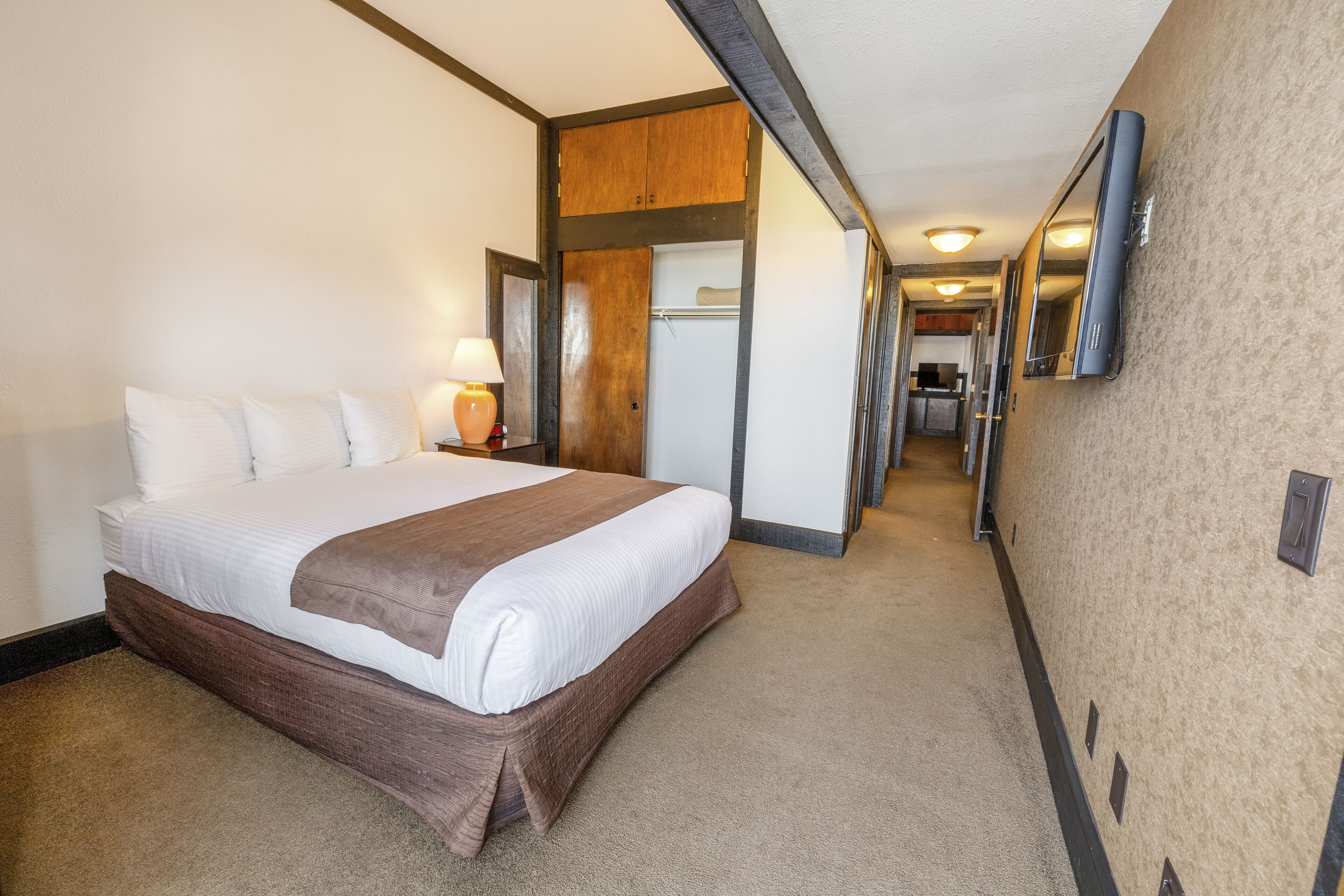 Una camera d'albergo con un letto grande, una lampada da comodino, un armadio in legno, uno specchio e un pavimento con moquette.