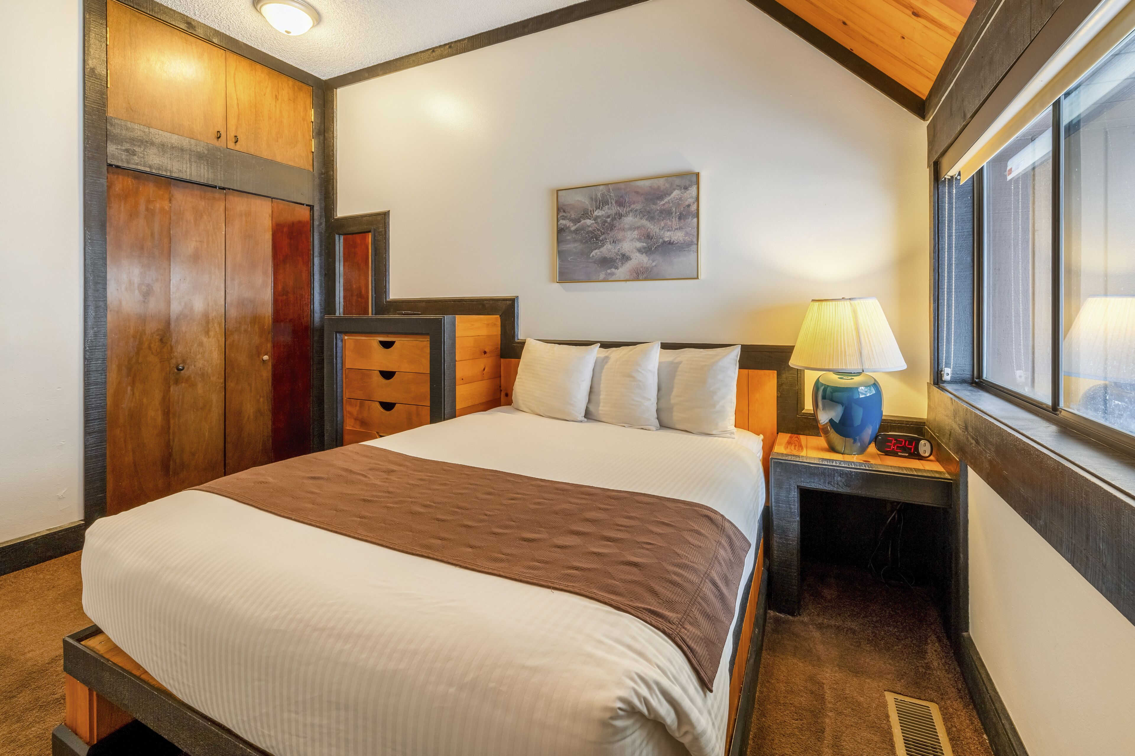 Een hotelkamer met een groot bed, een houten garderobe, een nachtkastje met een lamp, en een raam met uitzicht.