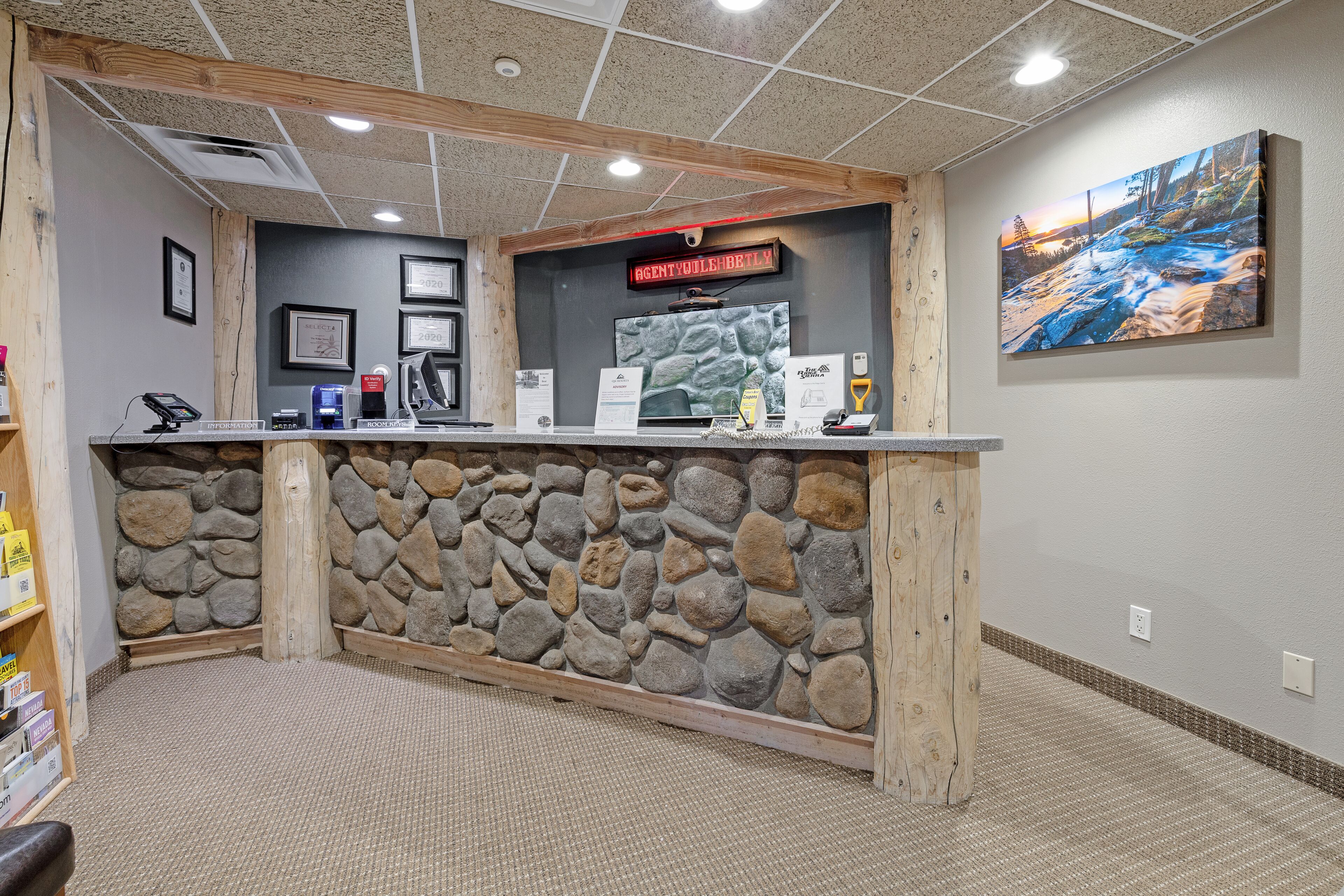 Un mostrador de recepción con un fondo de pared de piedra, diplomas enmarcados y una pantalla digital.