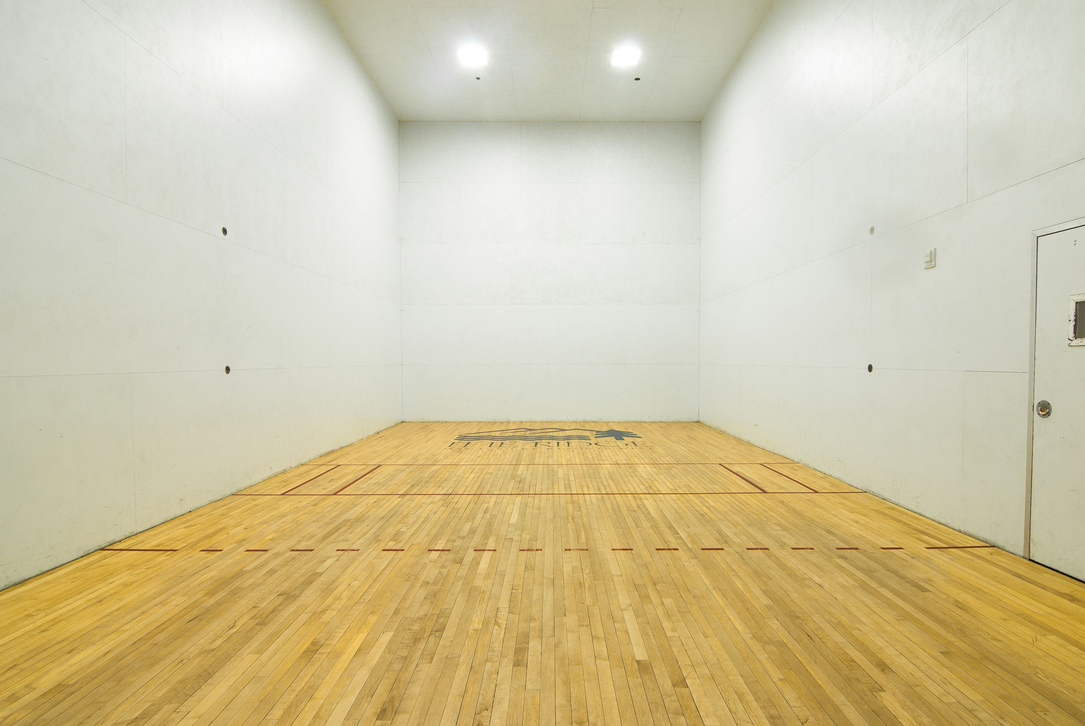 En squashhall med trägolv och vita väggar.