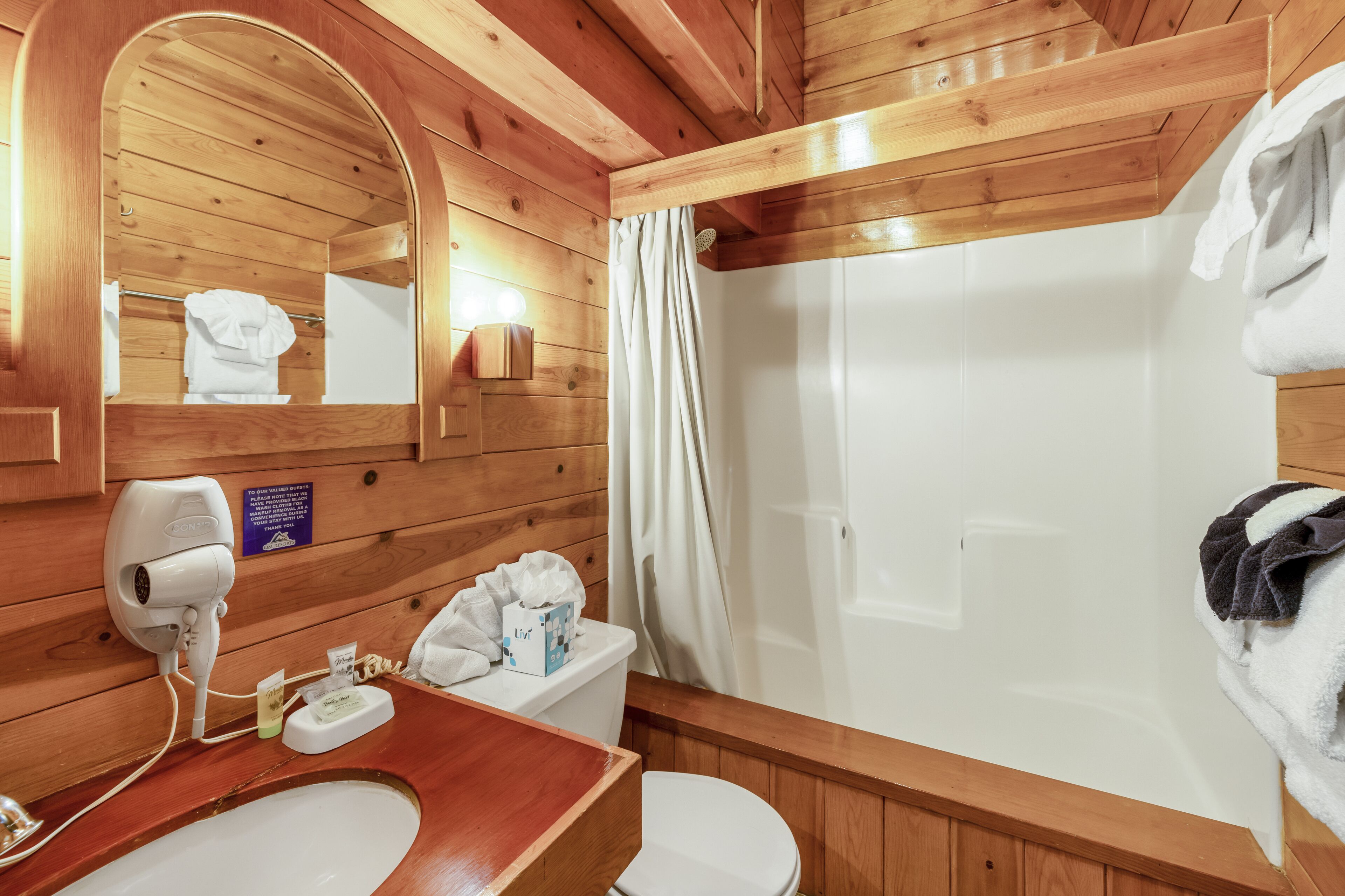 A wooden bathroom with a sink, toilet, and shower.