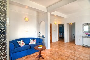 Ein Wohnzimmer mit einem blauen Sofa, einem runden Holztisch mit Obst und einer dekorativen Wandleuchte.