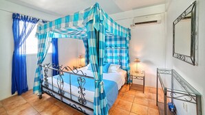 A room with a bed, a nightstand, a mirror, and a window with curtains. - Caribbean Sea View Holiday Apartments (Mero)