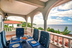 A balcony with a table set for dining, overlooking a scenic view of the sea and greenery. - Caribbean Sea View Holiday Apartments (Mero)