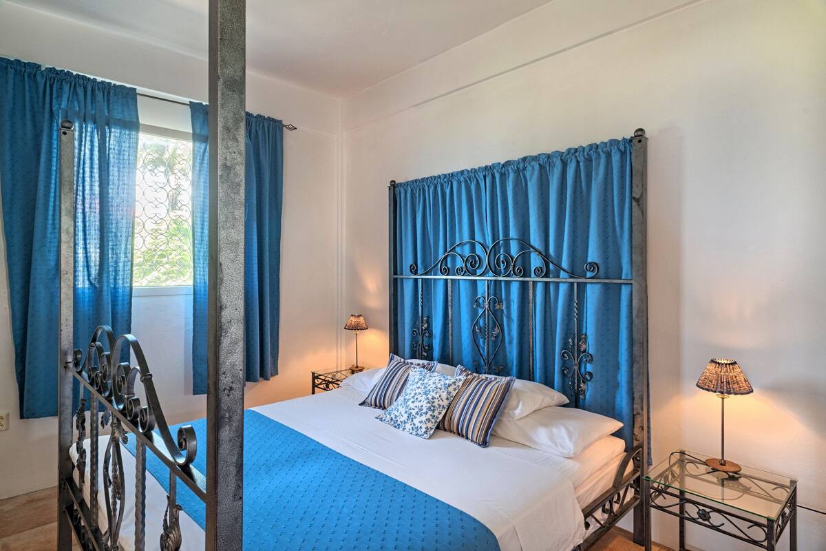 A bedroom with a bed, curtains, a metal headboard, two bedside lamps, and a window with a view.