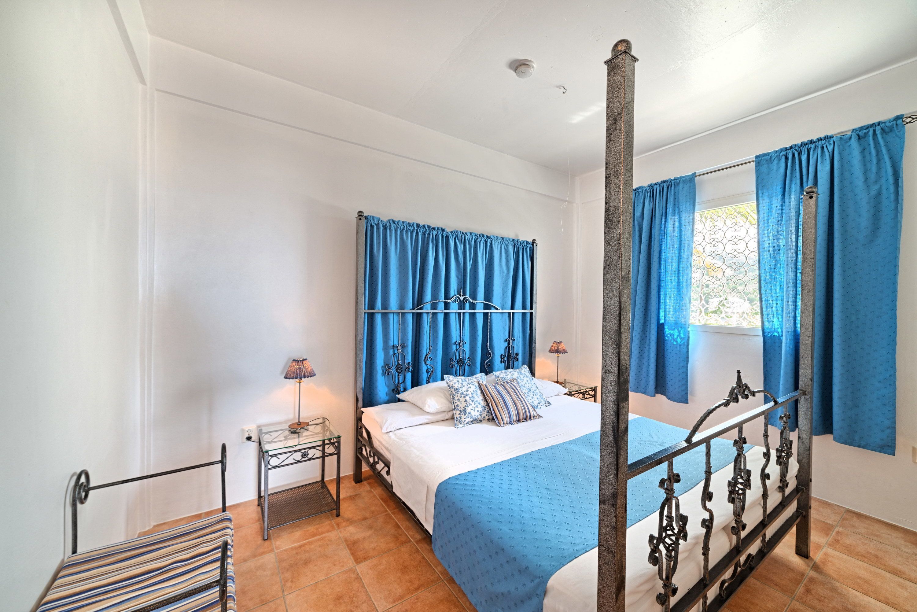 A bedroom with a four-poster bed, a nightstand, and a window with curtains.