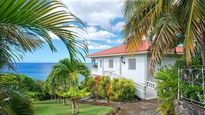 A white house with a red roof, surrounded by tropical plants and a view of the ocean. - Caribbean Sea View Holiday Apartments (Mero)