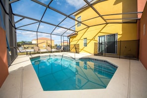 An indoor swimming pool with clear blue water, surrounded by a glass enclosure, and adjacent to a yellow building with a red roof. - Bella Vida Resort by Home 2U (Kissimmee)