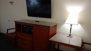 A hotel room with a wooden desk, a chair, a microwave, a television, and a lamp. - Hurricane Inn (Waynesboro)