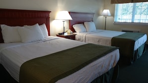 A hotel room with two beds, each with white linens and a green blanket. There are bedside lamps, a telephone, and a window with blinds. - Hurricane Inn (Waynesboro)