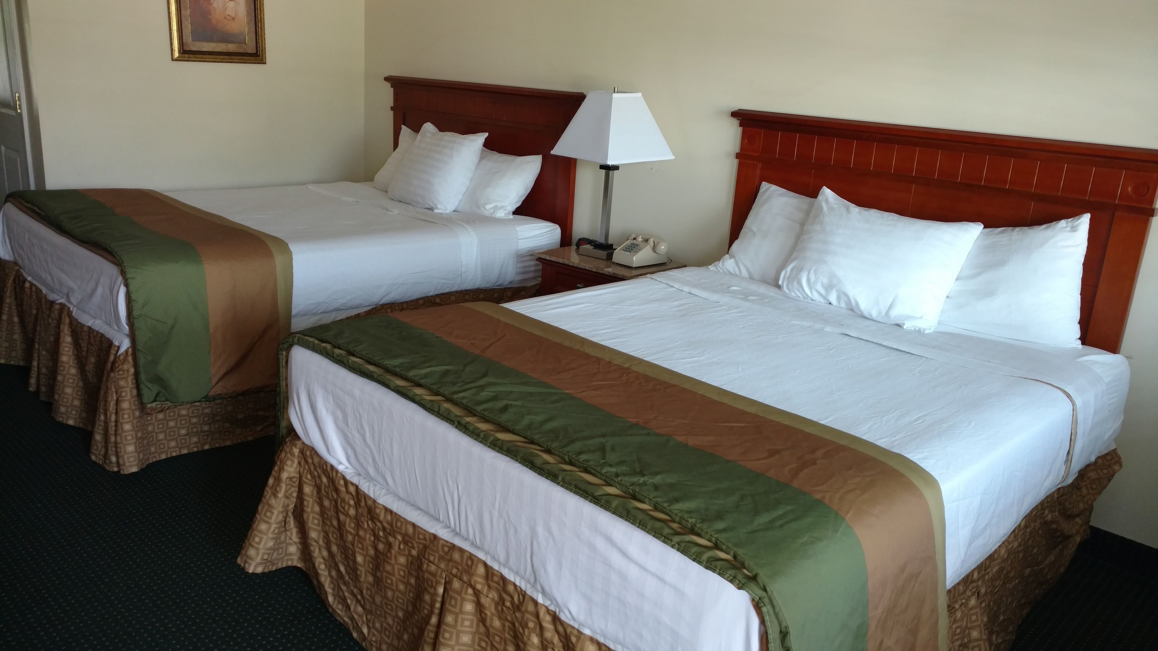 Two double beds with wooden headboards, white linens, and green and brown bedspreads.