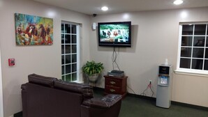 A room with a leather sofa, a television mounted on the wall, a fire alarm, a potted plant, and a water dispenser. - Hurricane Inn (Waynesboro)