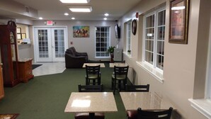 A room with a green carpet, a sofa, a table with chairs, a clock on the wall, and a door with an EXIT sign. - Hurricane Inn (Waynesboro)