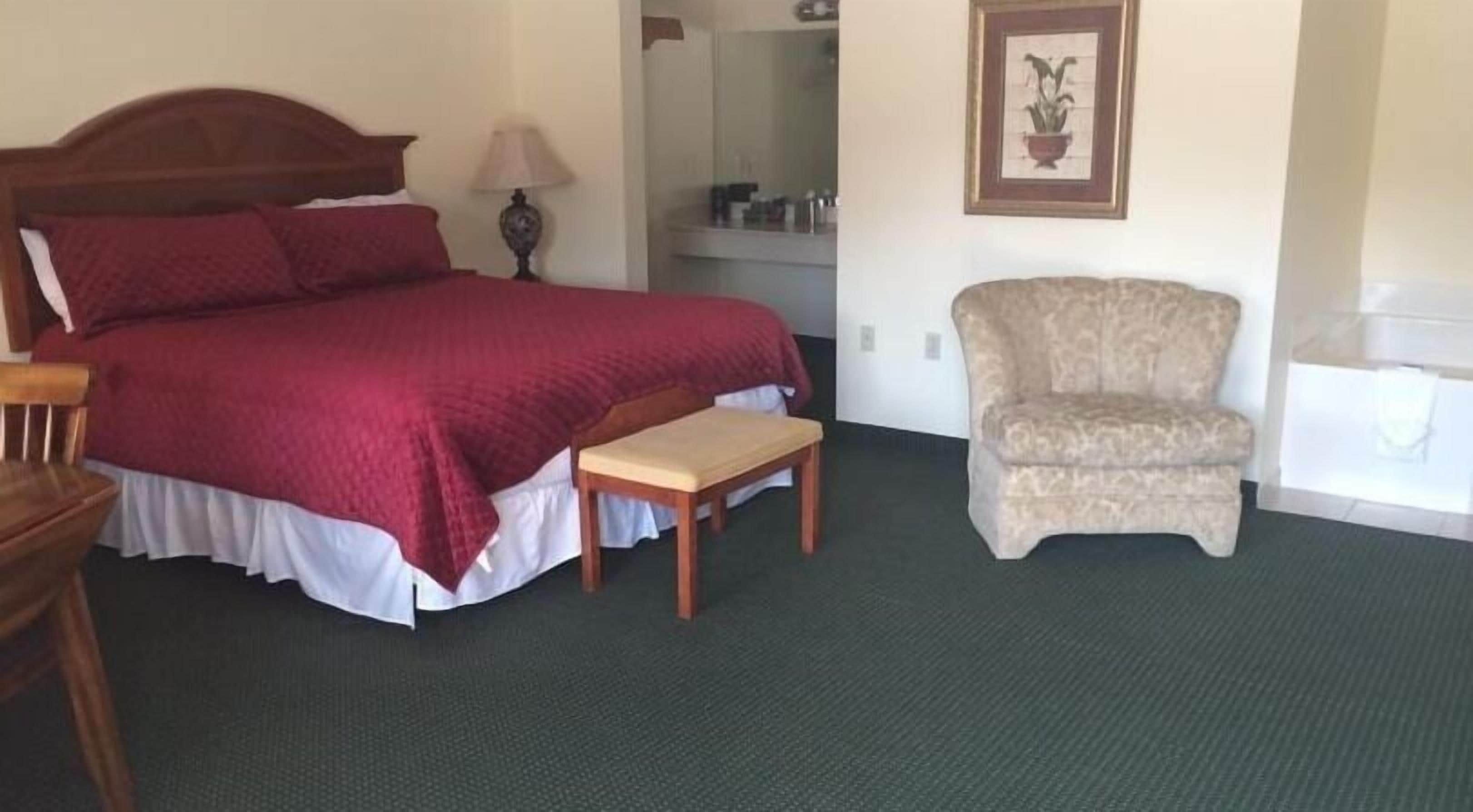 Ein ordentlich eingerichtetes Hotelzimmer mit einem großen Bett, einem kleinen Tisch, einem Sessel und einem Spiegel.