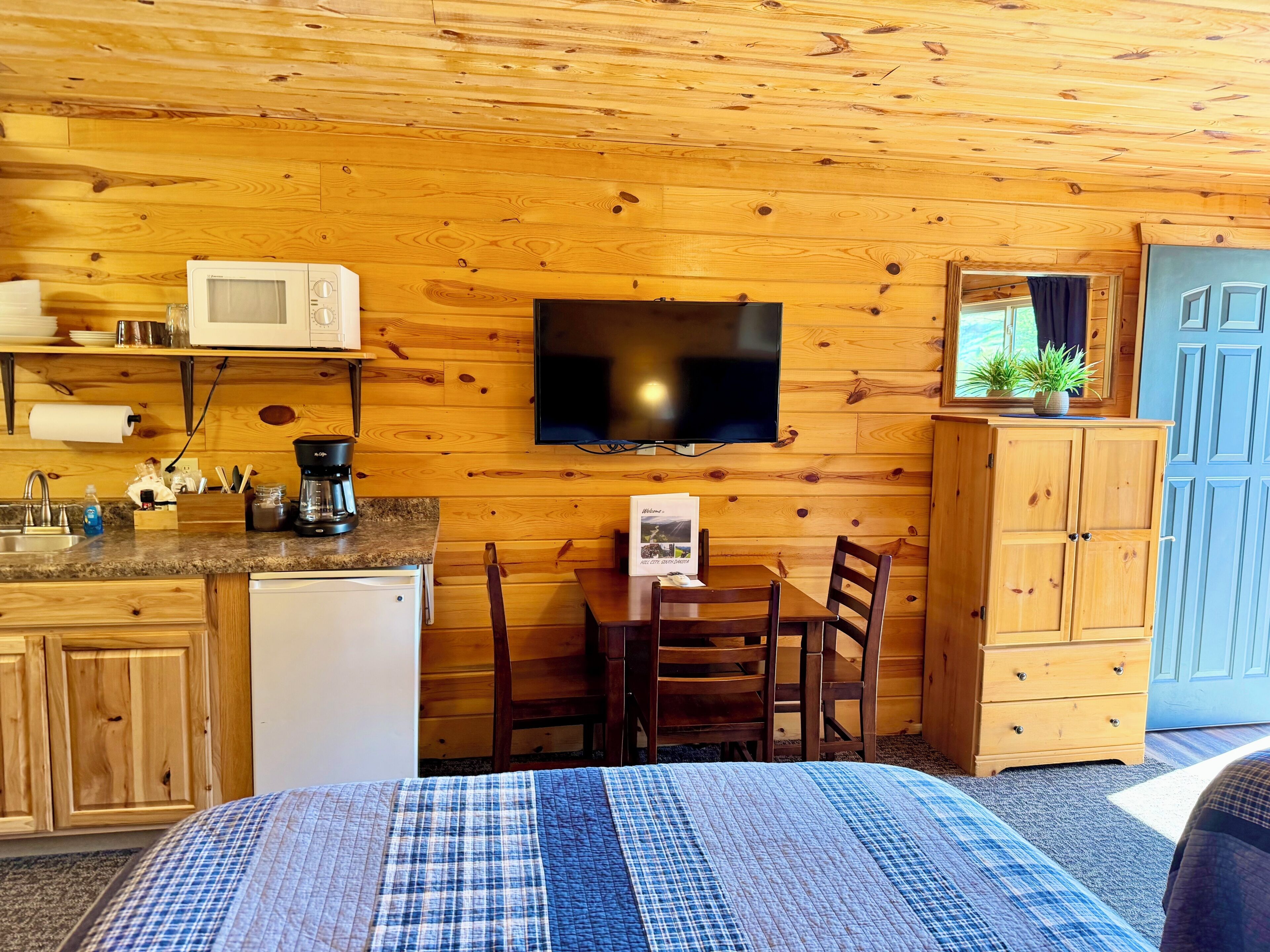 Une pièce confortable avec un lit, un mur en bois, une télévision, une petite table avec des chaises et un meuble.