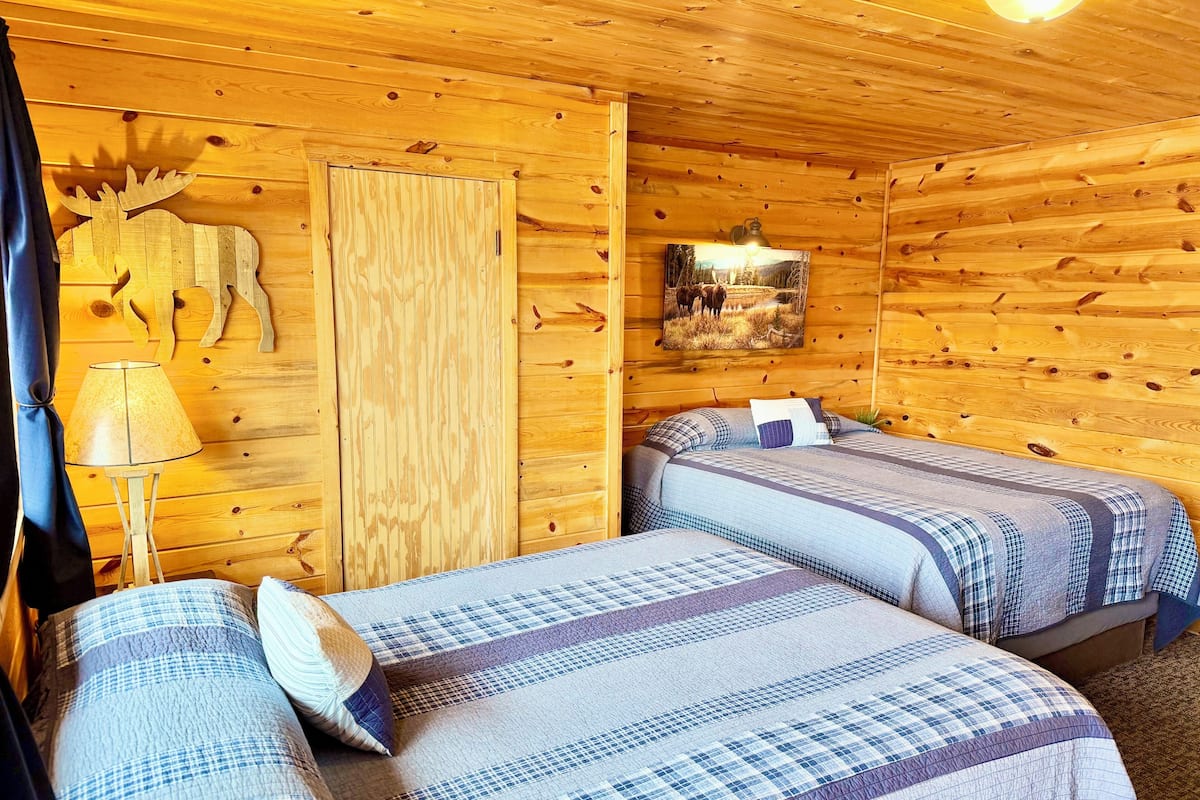 Une chambre de style chalet en bois, avec deux lits, une lampe, une décoration représentant un élan et un tableau encadré au mur.