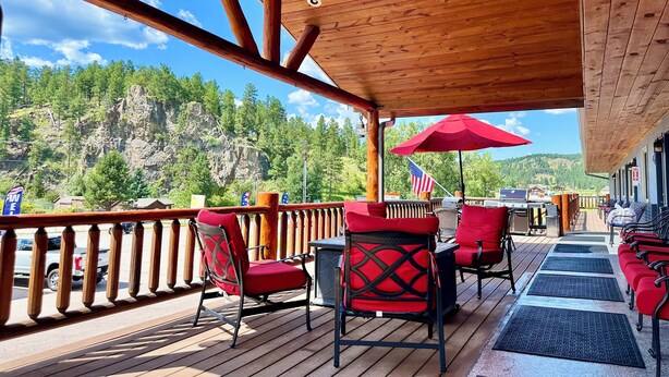 A wooden deck with outdoor seating, a view of a mountainous landscape, and an American flag. - Mountain View Lodge & Cabins (Rapid City)