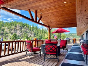 A wooden deck with outdoor seating, a view of a mountainous landscape, and an American flag. - Mountain View Lodge & Cabins (Rapid City)