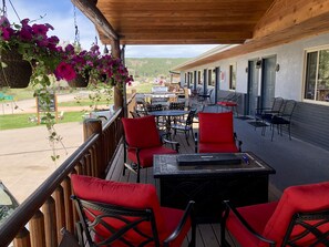 A covered outdoor seating area with red chairs and tables, overlooking a parking lot and a building with multiple doors. - Mountain View Lodge & Cabins (Rapid City)