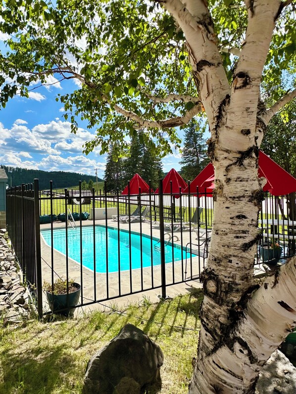 A swimming pool surrounded by a black metal fence, with red umbrellas and lounge chairs in the background. - Mountain View Lodge & Cabins (Rapid City)