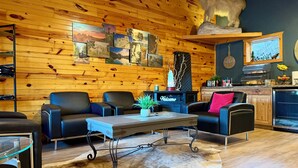 A cozy room with wooden walls, a leather sofa, a coffee table, and a mounted animal head. - Mountain View Lodge & Cabins (Rapid City)