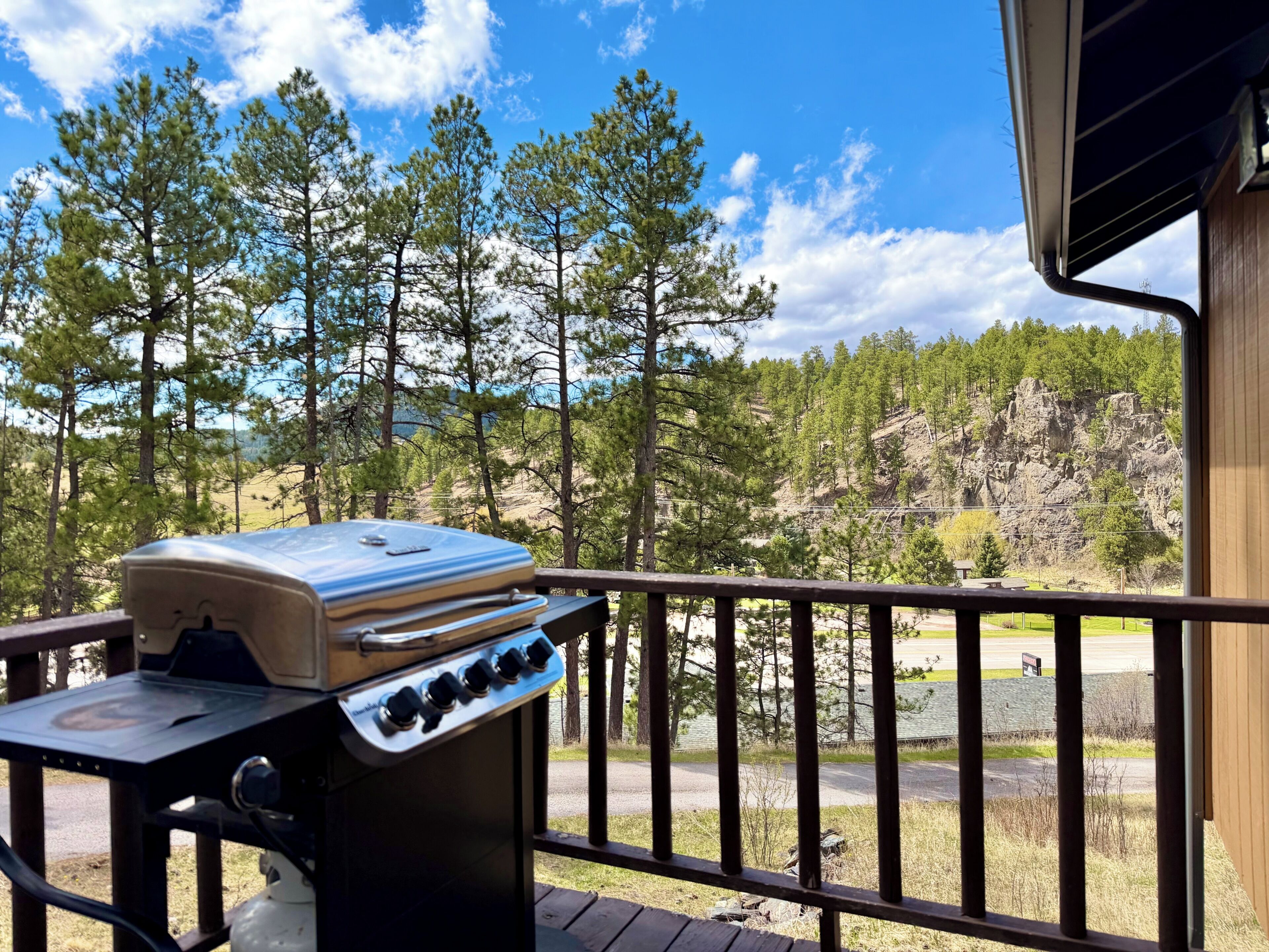 Un barbecue sur un balcon avec vue sur les arbres et une colline rocheuse.