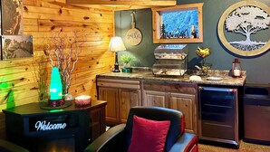 A cozy cabin-style room with a wooden ceiling, a mounted animal head, a fireplace, a bar area, and a 'Welcome' sign. - Mountain View Lodge & Cabins (Rapid City)