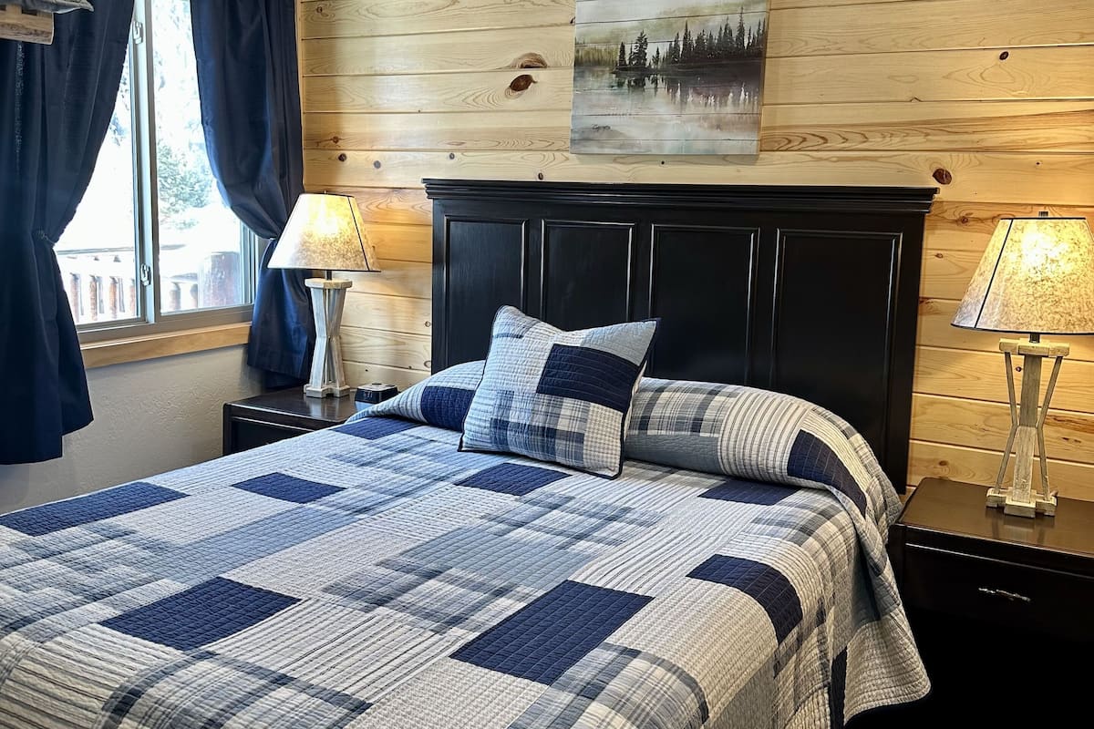 Une chambre avec un grand lit, des murs recouverts de panneaux de bois, un tableau et deux lampes de chevet.