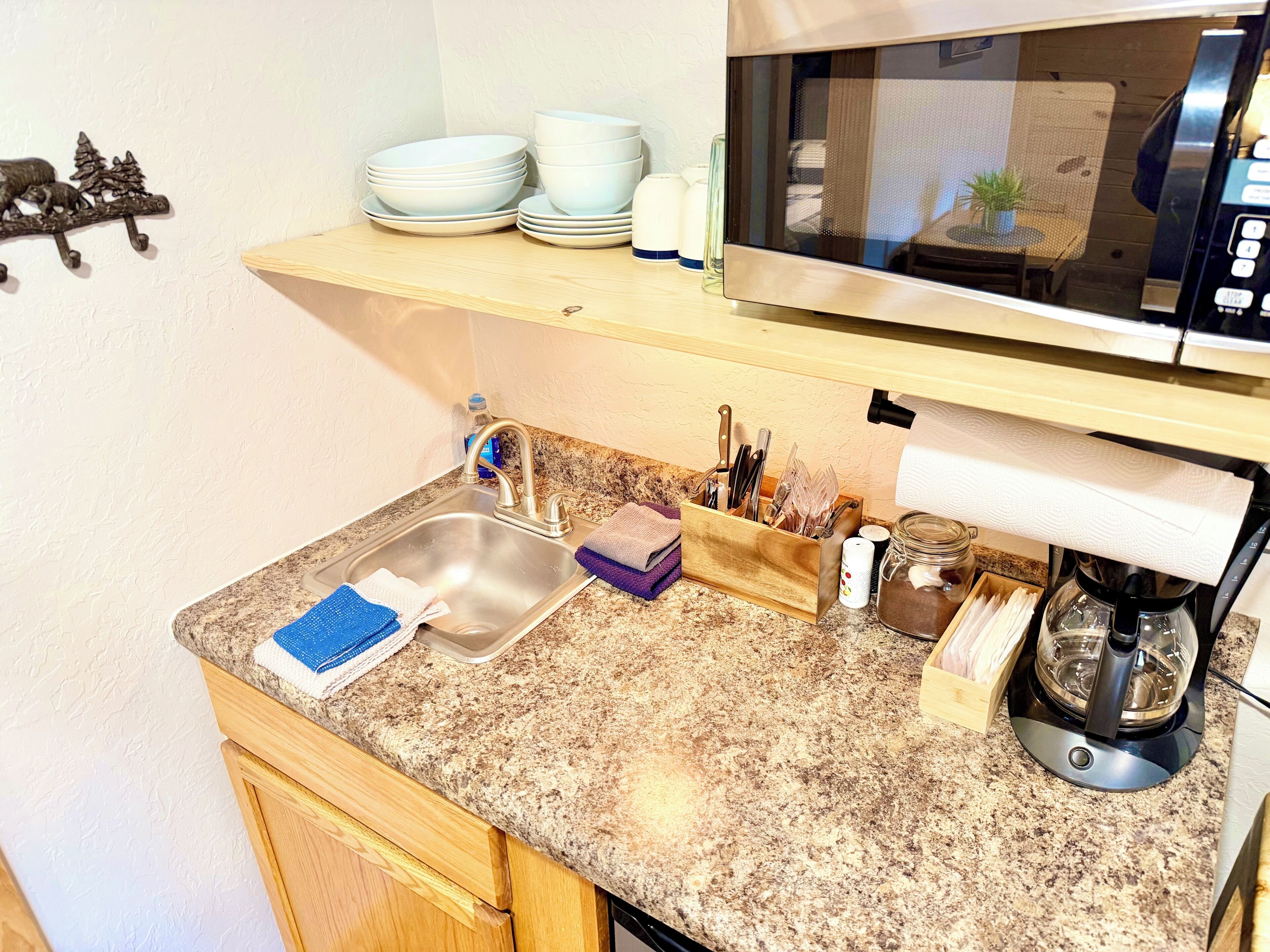 Una cocina con un lavabo, microondas y diferentes utensilios.